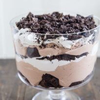 A square photo showing the Oreo Brownie Trifle from the side, showcasing the layers of brownie chunks, chocolate pudding, whipped topping and the crumbled Oreos.